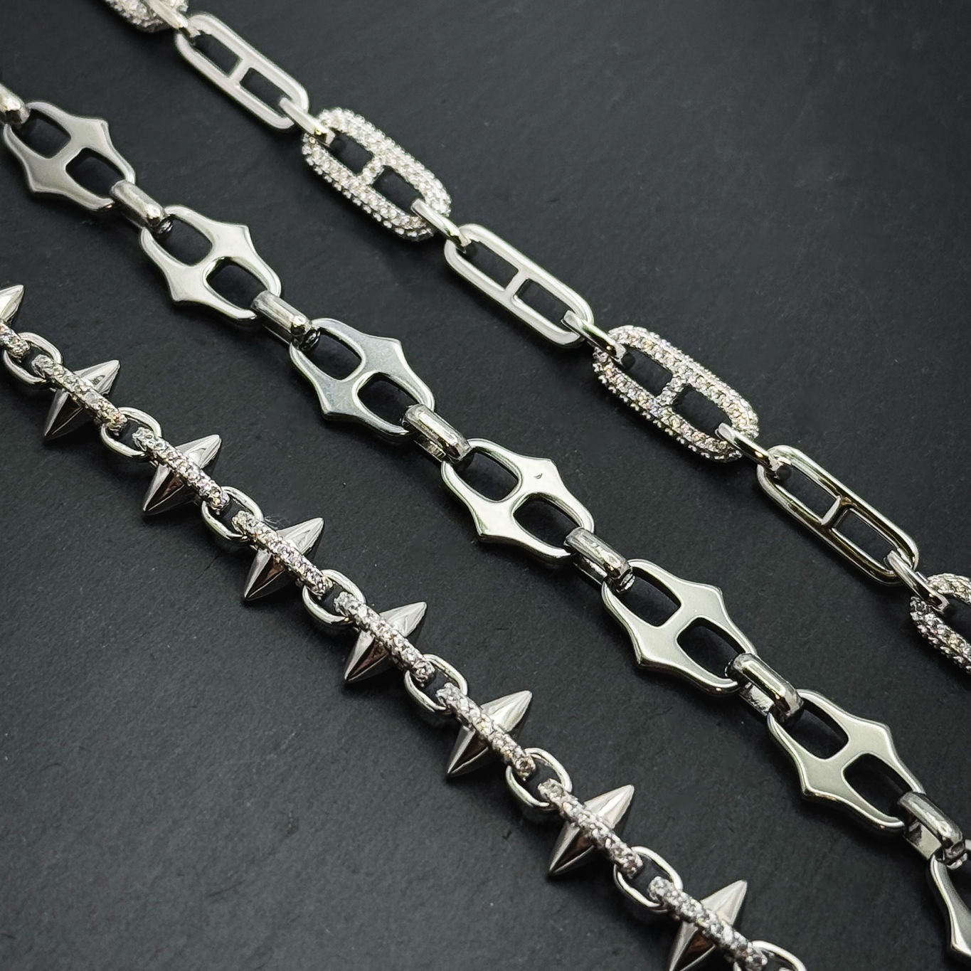 Three sterling silver chains on black slate: pavé links, sculpted links and a spiked chain